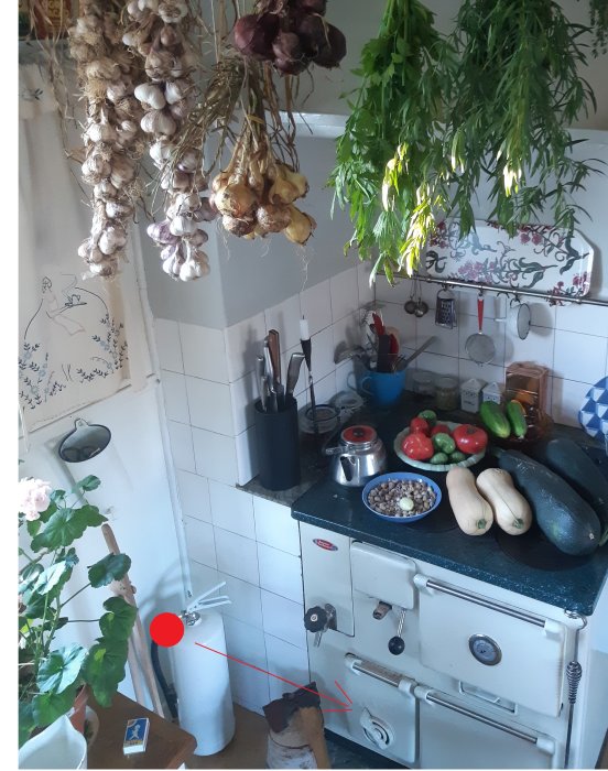 Kök med torkade örter upphängda och vintage spis, röd markering pekar på plats nära golvet.