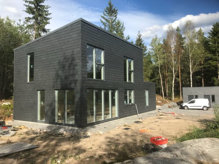 Nybyggt unikt hus med skifferfasad och stora fönster, under konstruktion på en tomt.