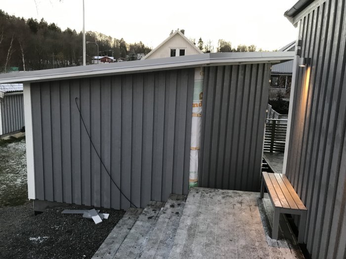 Halvfärdigt bygge med nyinstallerad grå panel och insatta fönster, synligt byggmaterial.