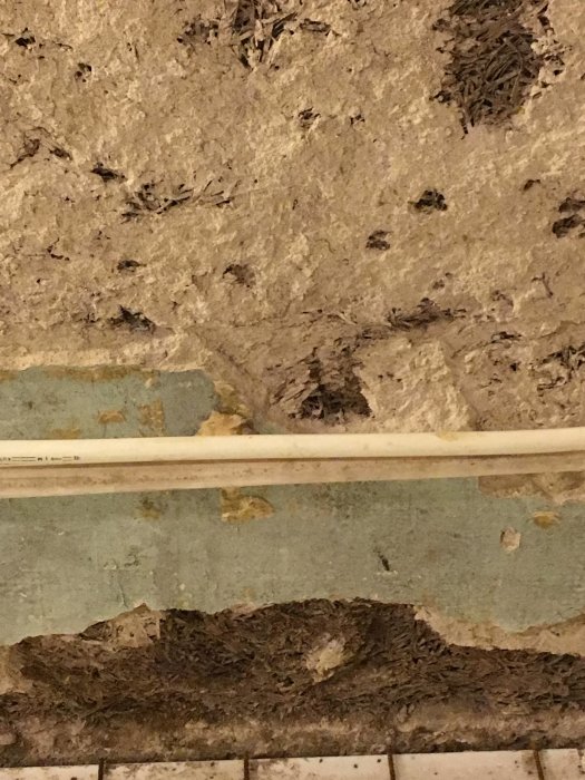 Delvis exponerad vägg med träullit, porös puts och rörläggning, i ett renoveringsprojekt.