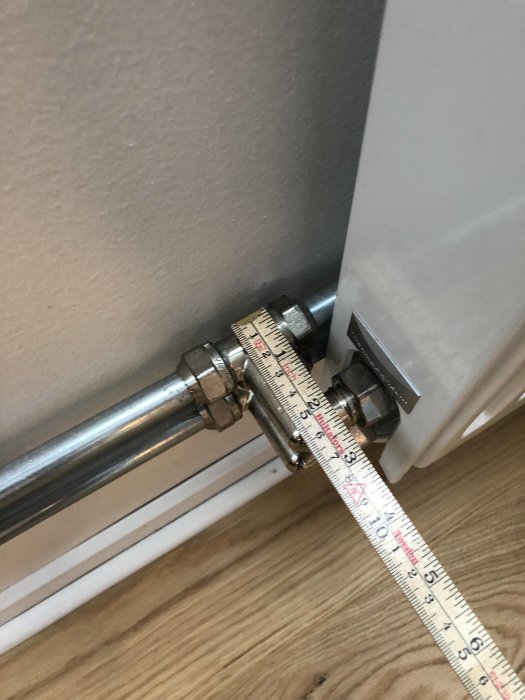 Mätmått som mäter avstånd mellan golv och anslutning på radiator med rördetaljer.