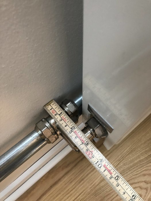Koppling till radiator med mätande tumstock som visar avståndet mellan rör och golv.