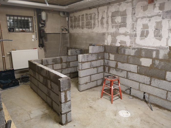 Byggnation av Leca-skalmur i källare med synliga rör och installationszoner.