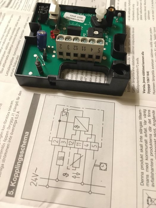 Öppen rumstermostat med synliga elektroniska komponenter ovanför ett kopplingsschema.