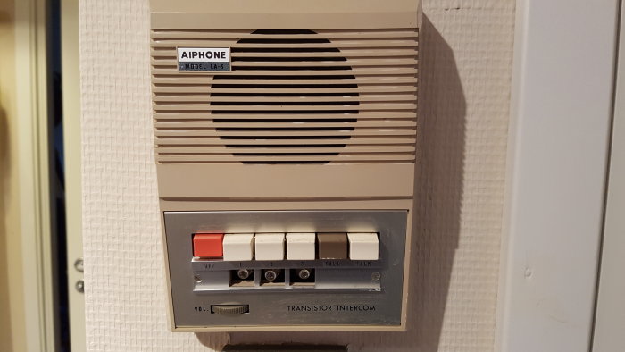 Vintage AIPHONE intercom system med knappar för samtalsalternativ på en vägg, liknar ironiskt en telefonmodell.