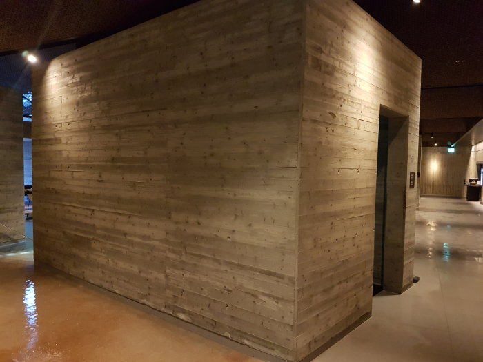 Betongväggar med träplankstruktur och reflektioner på golvet i ett spa.