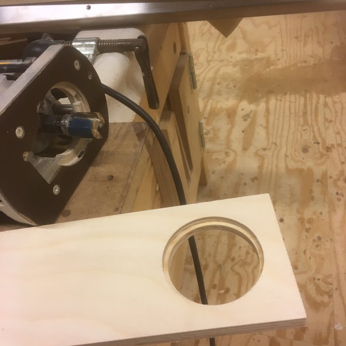 Träbit med utfräst cirkulär fördjupning vid sidan av ett fräsbord och verktyg på ett arbetsbord.