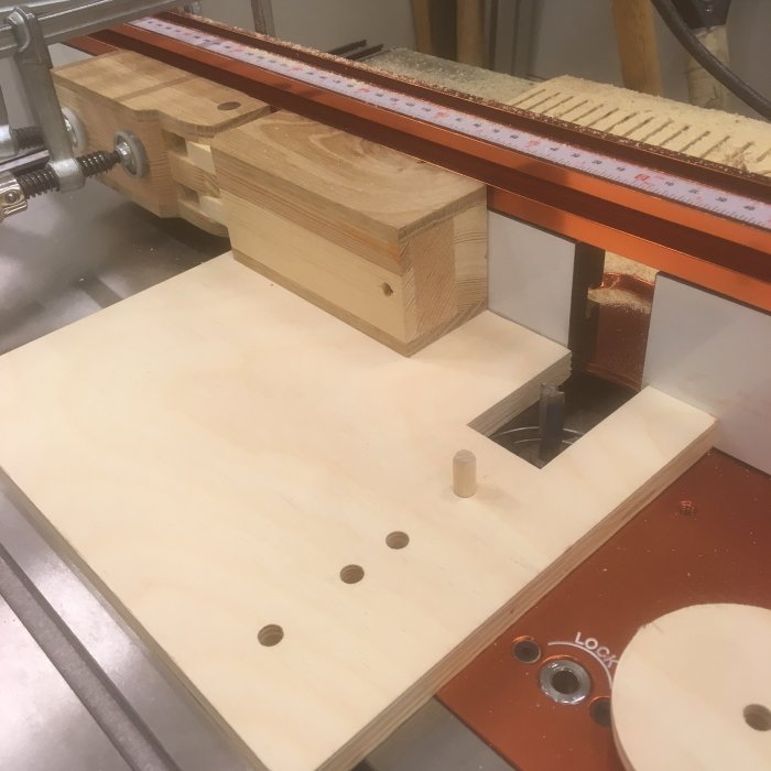 Woodworking jig setup on router table with timber pieces and adjustment mechanism.