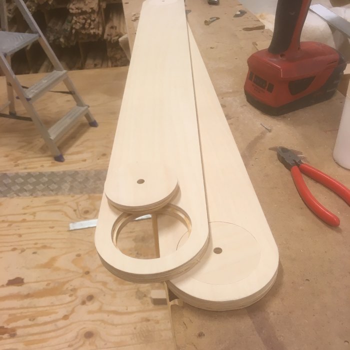 Träkomponenter på en arbetsbänk med utfrästa cirklar och hål, nära snickeriverktyg.