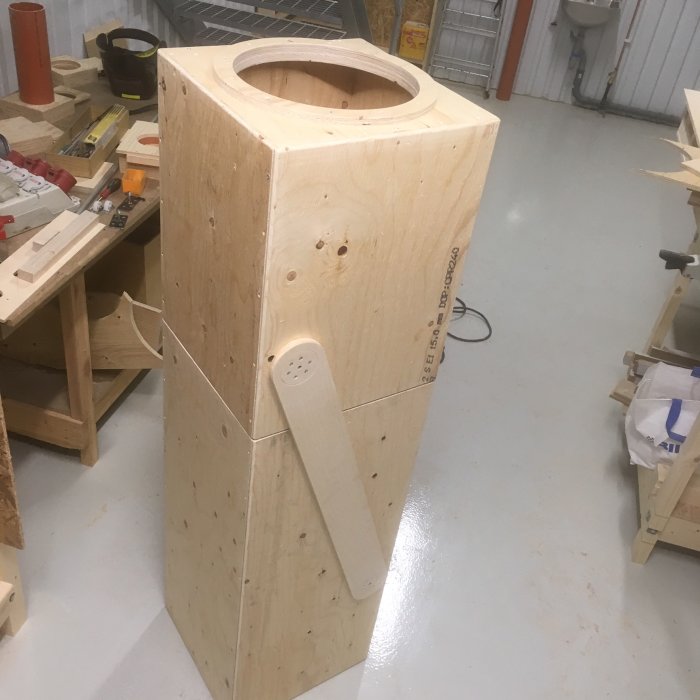 Hantverksprojekt av trä med konstruerade länkarmar och centralt hål, placerat i en verkstadsmiljö.