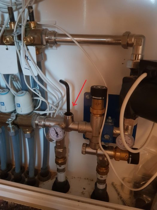 Ventil i ett golvvärmesystem mellan rör, mätare och ledningar, markerad med röd pil.