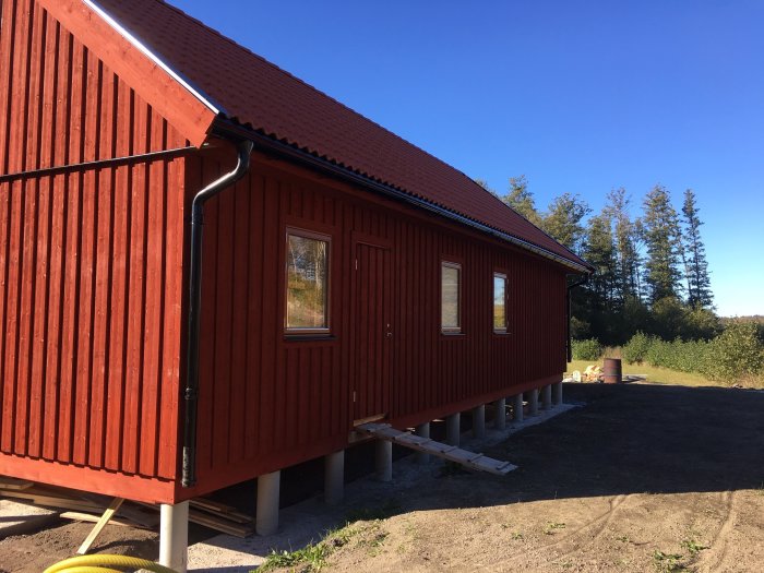 Rödmålat trähus på gjuten grund med betongsulor och plintar, stort tomrum runt huset.