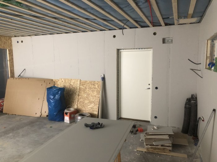 Inre delen av ett garage under renovering med isolerade väggar delvis täckta av OSB och gipsplattor, samt fördragen elkabel.