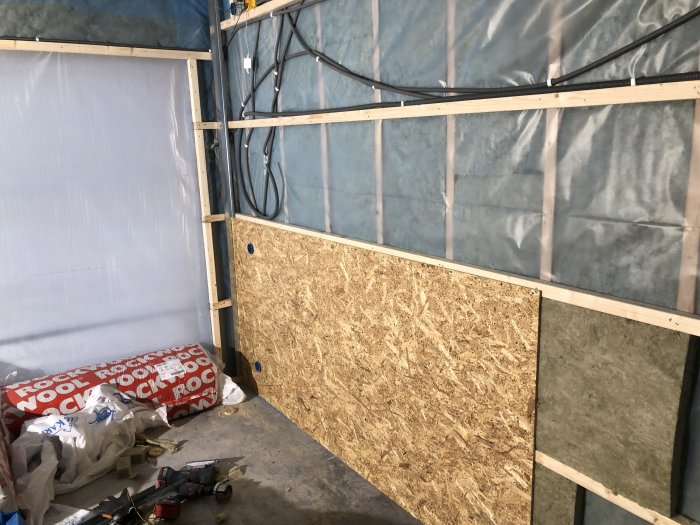 Garage under konstruktion med isolering, OSB-skivor, elinstallationer och byggmaterial på golvet.