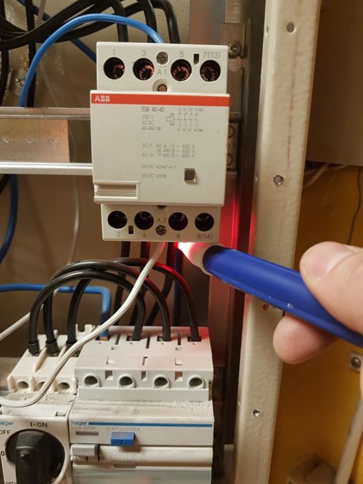 En person testar strömmen på ett relä i en elcentral med en spänningsprovare som lyser rött.