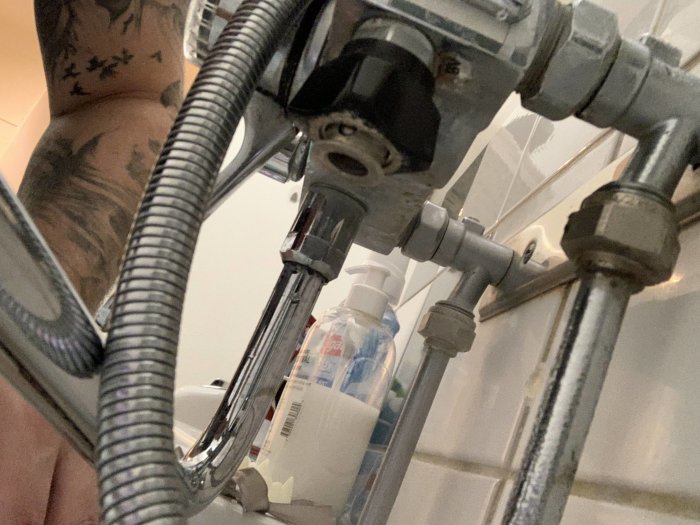 Otydlig bild på en vattenkran och rör under en diskbänk med en synlig snabbkoppling och flexibel vattenslang.