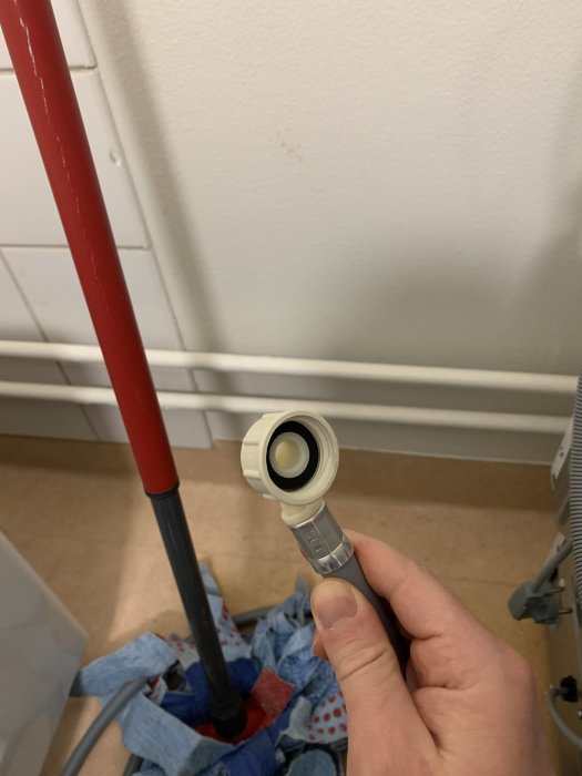 En hand håller en tvättmaskins vattenslang med oidentifierad snabbkoppling.