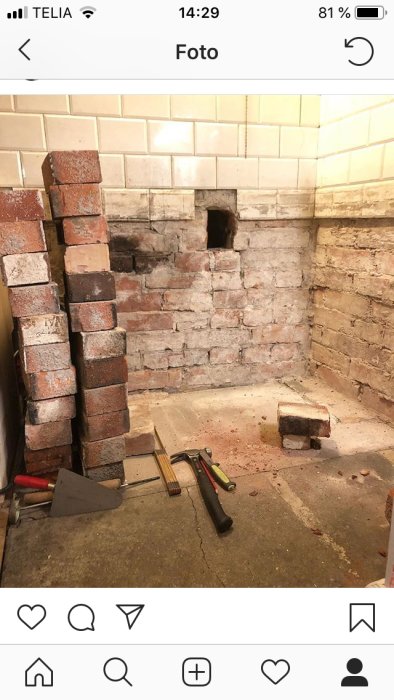 Orenoverat hörn av ett rum med tegelväggar och murverk, redskap för murning och en öppning för en vedspis.
