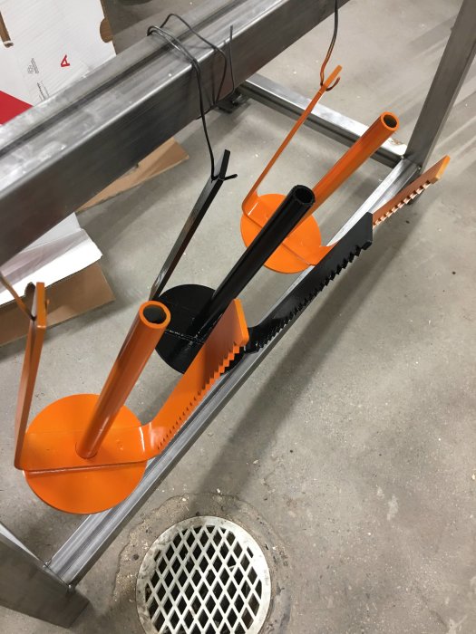 En handsåg och två rörskärare med orange handtag som ligger på ett metallställ i en verkstad.