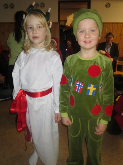 Två barn utklädda till Lucia och en julgran, med hemmagjorda kostymer, vid ett firande.