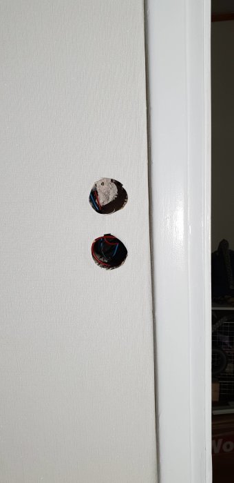 Två hål i en vit vägg med synliga elledningar, tänkt för eluttag eller strömbrytare.