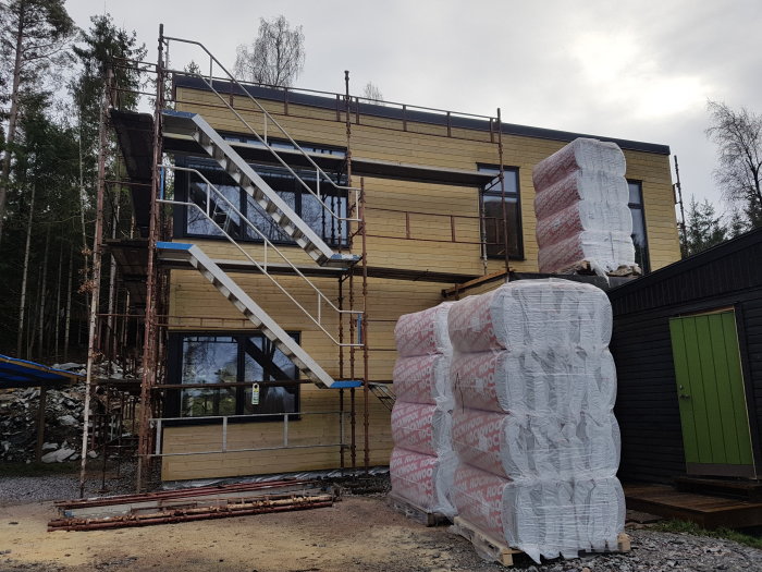 Delvis renoverat hus med ställning och flera balar isolering framför.