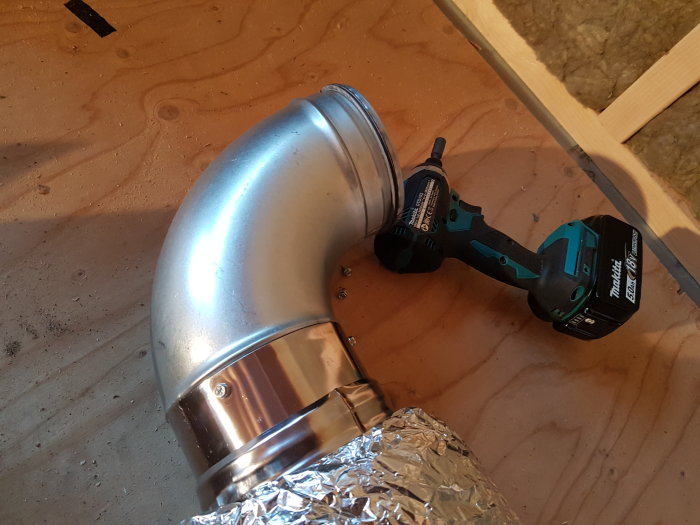 Ventilationsrör och bockad armbåge med isolering i bakgrunden, bredvid en Makita skruvdragare.
