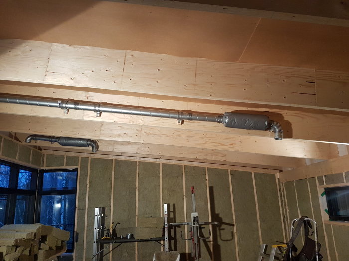 Ventilationsrör installerade mellan takbalkar, isolerade väggar och plast i taket i en byggkonstruktion.