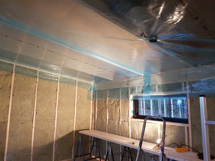 Isolerat rum med installerad plastångspärr i taket och isolering mellan väggstolpar.