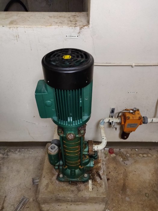 Grönmålad vattenpump och filterenhet monterade på betongplatta i ett pumphus med fråga om underhåll.