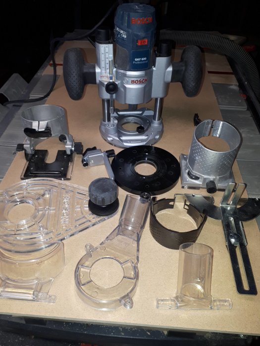 Bosch GKF 600 fräs med tillbehör som sänkenhet och olika genomskinliga skyddsluckor spridda på ett arbetsbord.