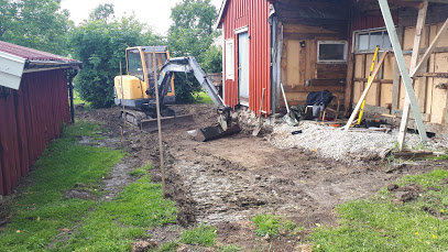 Minigrävare vid husgrund som utför grävningsarbete för renovering, med grushög och stegar.