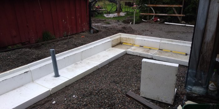 Nygrävd grund med vita betongblock och nivåmätning vid ett byggprojekt utomhus.