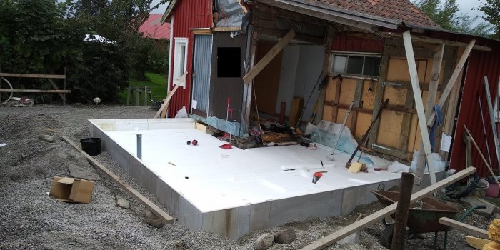 Grundläggning av hus med isolering och betongplatta, byggmaterial och verktyg runtomkring.