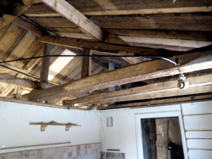 Öppet tak med exponerade träbjälkar och spikar där ett innertak tidigare varit fäst, i en under renovering.