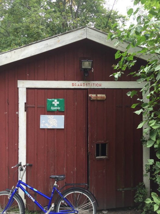 Röd träbyggnad med skylt som säger "BRANDSTATION" och en cykel parkerad framför.