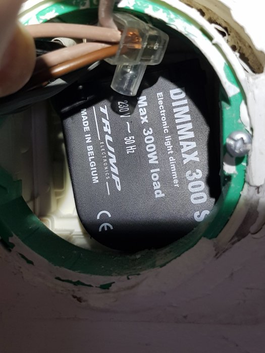 Närbild av en elektronisk dimmer för ljus i ett vägguttag med kablar och en märkning som visar specifikationer.