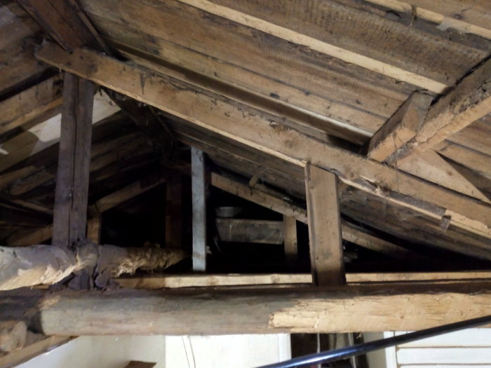 Bild på träbjälkar och takkonstruktion under renovering i ett hus med synlig taklutning.