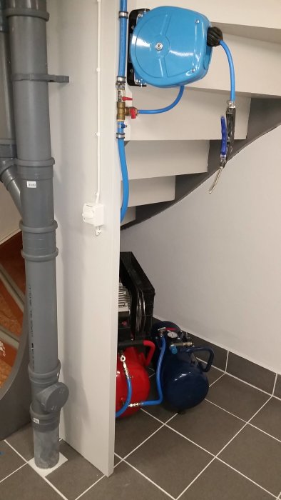 Ny målad källartrappa med kompressor och slangvinda installerade under trappan.