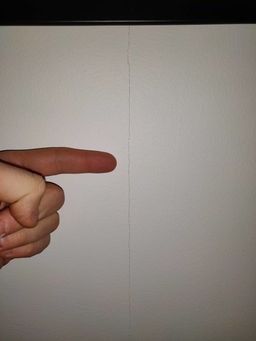 Person pekar på en vertikal spricka i en vitmålad vägg där ett fönster tidigare varit placerat.