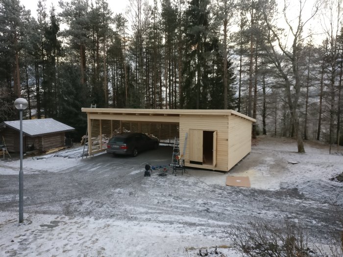 Nybyggd trägarage med nästan komplett träpanel och bifogad carport i vintertid.