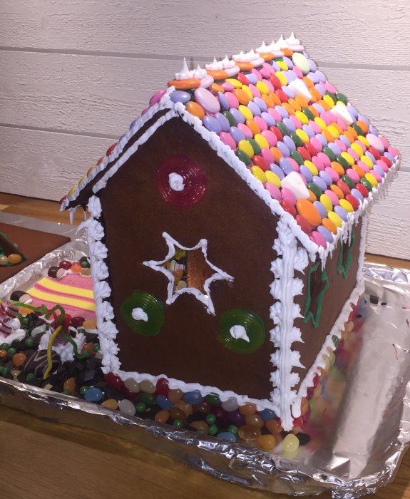 Hemmagjort pepparkakshus dekorerat med färgglatt godis, sockerglasyr och omgiven av lösgodis.