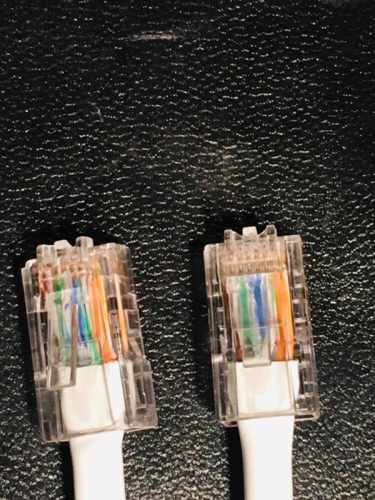 Två RJ45-nätverkskontakter med synliga färgkodade kablar mot en svart texturerad bakgrund.