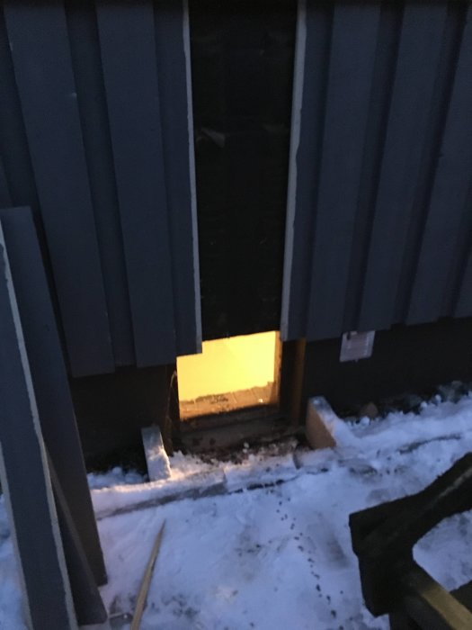 Fasadöppning med insatt ränna runt hus på vintern med snö på marken och verktyg synliga.