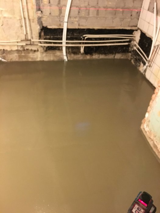 Nyutgjuten betonggolv med synliga rör på vägg och mätinstrument i förgrunden.