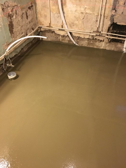 Nyligen utslagen betonggolv med synliga rör och wires, ojämn vägg efter modifiering.