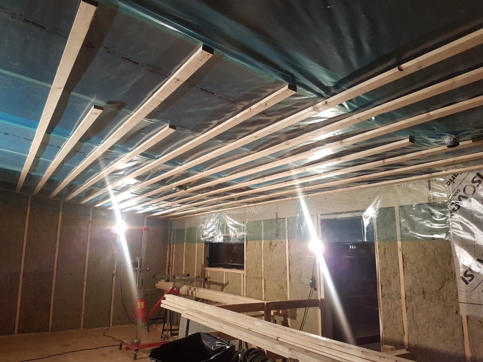 Byggarbetsplats med spikad läkt i taket, isoleringsmaterial på väggar och rullställning i bakgrunden.