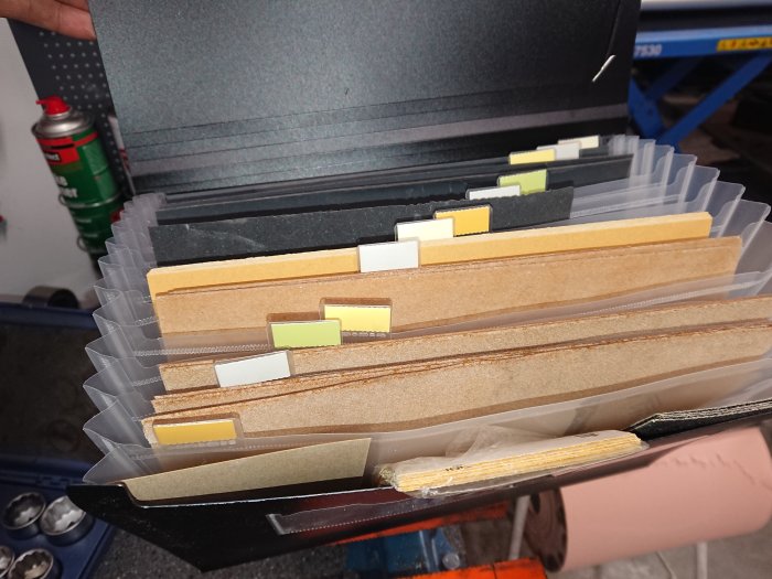 Öppen verktygslåda som innehåller ordnade slipark av olika grovhet organiserade i plastfickor.