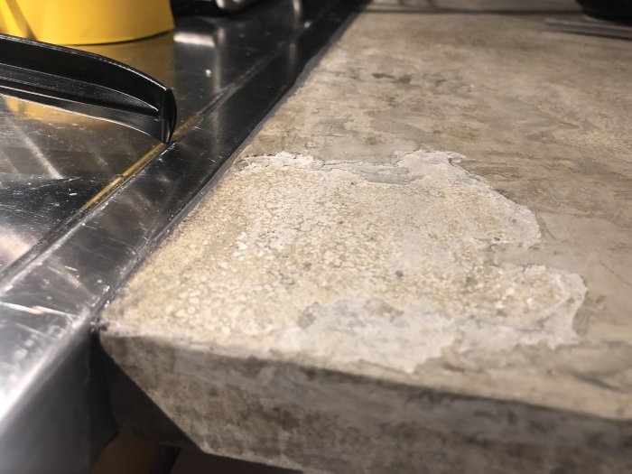 Reparationsområde på en grå betongköksbänk där en patch av slurry har lossnat vid hörnet nära en diskho.