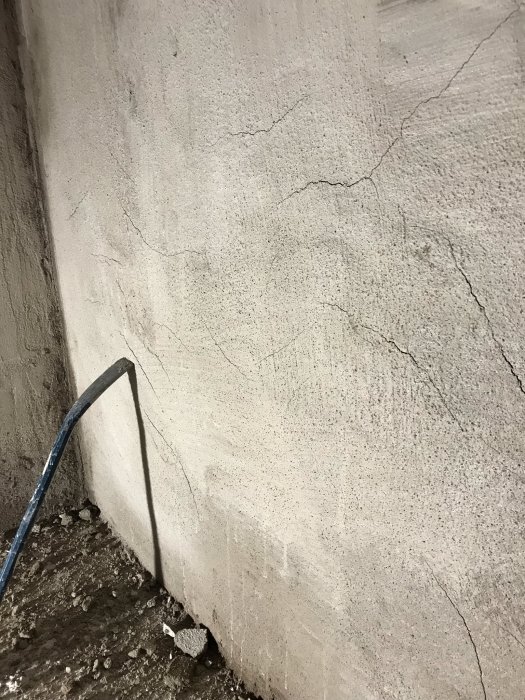 Putsad källarvägg med sprickbildning och ojämnheter, sista metern på en renoveringsprojekt.